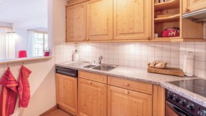 A kitchen with wooden cabinets, a stainless steel sink, a stove, and a window with curtains. - Alprüüsch, Obersaxen-Misanenga, (Obersaxen), 34155B by Interhome (Obersaxen Affeier)