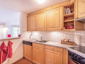 A kitchen with wooden cabinets, a stainless steel sink, a stove, and a window with curtains. - Alprüüsch, Obersaxen-Misanenga, (Obersaxen), 34155B by Interhome (Obersaxen Affeier)
