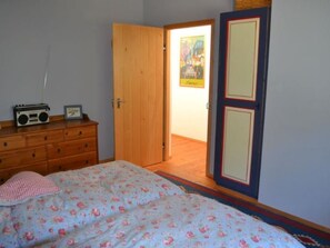Une chambre à coucher comprenant un lit, une commode, une radio et une porte donnant sur une autre pièce.