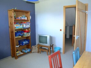 A room with a wooden bookshelf, a television on a stand, a red chair, and a wooden door leading to another room. - Ferienhaus Casa Patricia, Brigels, (Breil/Brigels), 65046B by Interhome (Breil/Brigels)