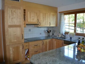 Une cuisine avec des meubles en bois, un plan de travail en granit et une fenêtre avec des rideaux.