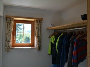 Une pièce avec une fenêtre, une étagère en bois et un portant à vêtements sur lequel sont disposés différents vêtements.