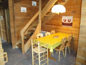 A wooden interior with a dining table, chairs, a staircase, and a wall-mounted poster. - Gadola, Obersaxen-Meierhof, (Obersaxen), 34069B by Interhome (Obersaxen Affeier)