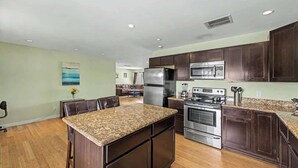 Una cocina con armarios de madera oscura, una isla de encimera de granito, electrodomésticos de acero inoxidable y un comedor con mesa y sillas.