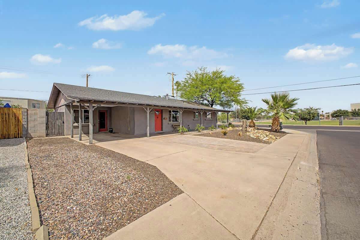 A single-story house with a front porch, a driveway, and a small garden with palm trees.