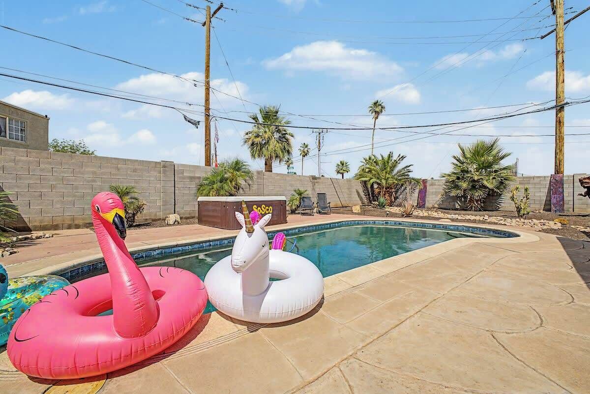 Una piscina con due galleggianti a forma di animale, un muro in mattoni e palme sullo sfondo.