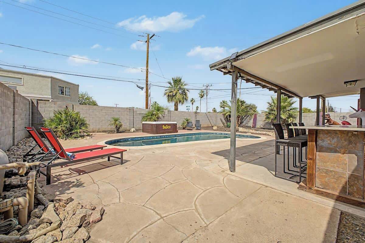 A backyard with a swimming pool, lounge chairs, a barbecue area, and a stone wall.