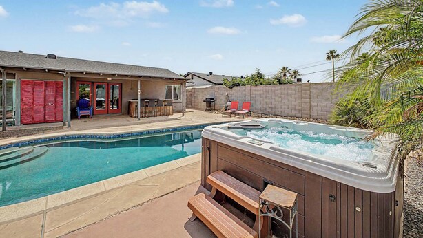 Un patio trasero con piscina, bañera de hidromasaje y un área de patio con sillas y una mesa.