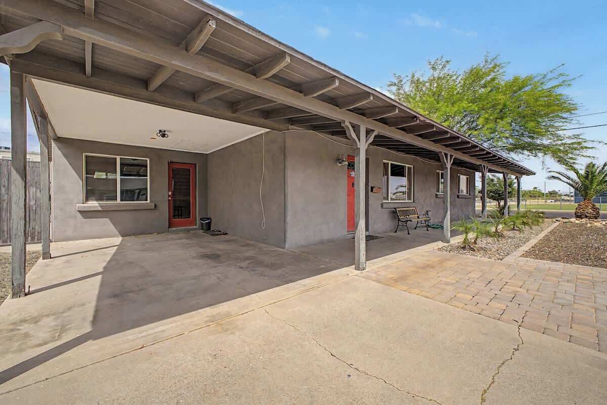 A single-story building with a covered patio, a red door, and a small outdoor seating area.