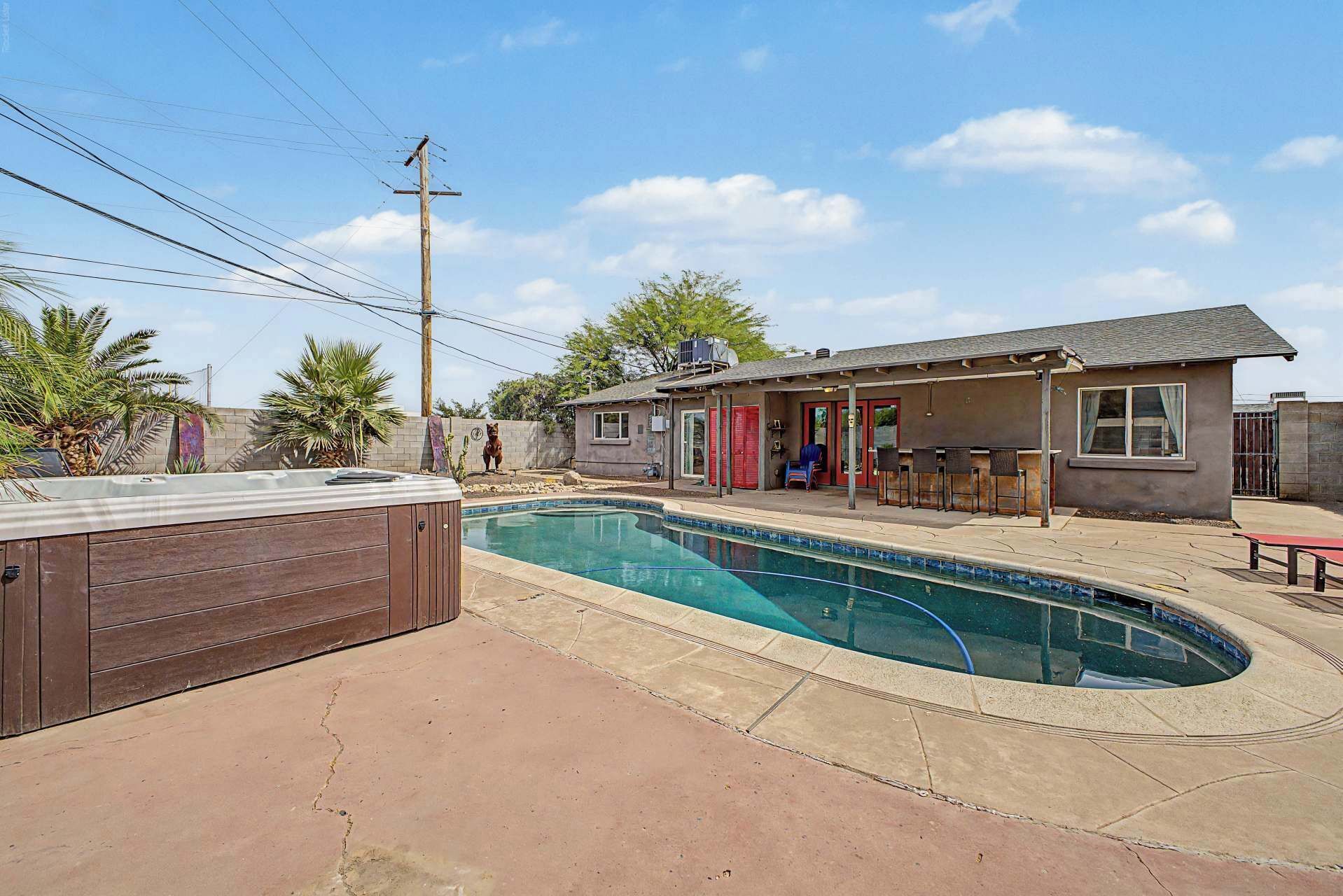 A residential swimming pool with a hot tub, a covered patio, and a small building with a bar area.