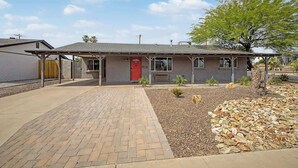 Una casa de un piso con puerta roja, porche cubierto y entrada pavimentada.
