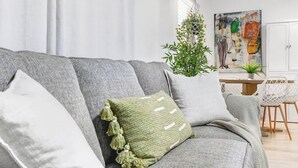 A grey sofa with a green pillow and tassels, a hanging plant, and a painting on the wall.