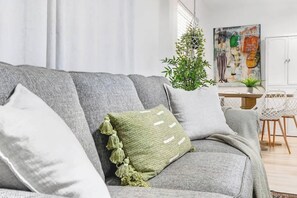A grey sofa with a green pillow and tassels, a hanging plant, and a painting on the wall.
