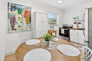 A modern kitchen with white cabinets, a dining table with placemats, and a painting on the wall.