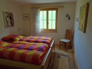 Une chambre à coucher avec un lit, une chaise, une fenêtre et des œuvres d’art accrochées aux murs.