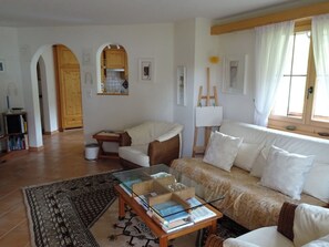 Un salon avec un canapé, un fauteuil, une table basse en verre et un tableau au mur.