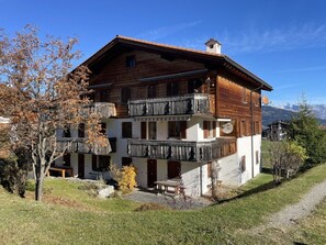 Ein zweistöckiges Holzhaus mit Balkonen, einem Steinweg und Blick auf Berge.