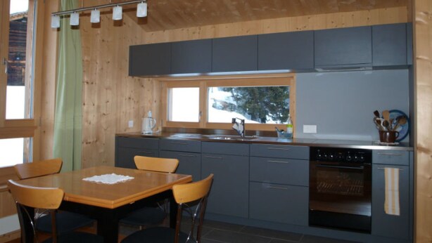 Una cucina moderna con pareti in legno, un tavolo da pranzo con sedie e una finestra vista alberi.