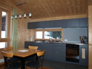 Una cocina moderna con paredes de madera, una mesa de comedor con sillas y una ventana con vistas a árboles.