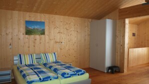 Una stanza con pannelli in legno, un letto, un armadio bianco e uno sgabello.