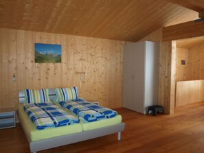 Una habitación con paneles de madera, una cama, un armario blanco y un taburete pequeño.