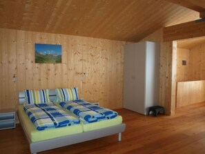 A wooden-paneled room with a bed, a white wardrobe, and a small stool.