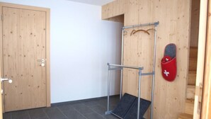 Una stanza con una porta in legno, una sbarra per trazioni in metallo, un tappetino rosso con una croce bianca e una scala.