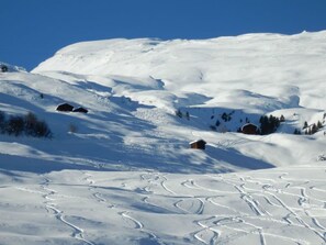 A snowy landscape with ski tracks, a small cabin, and a clear blue sky.