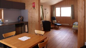 Un interno in legno con un tavolo da pranzo, sedie, angolo cottura, una finestra e una poltrona con cuscino.
