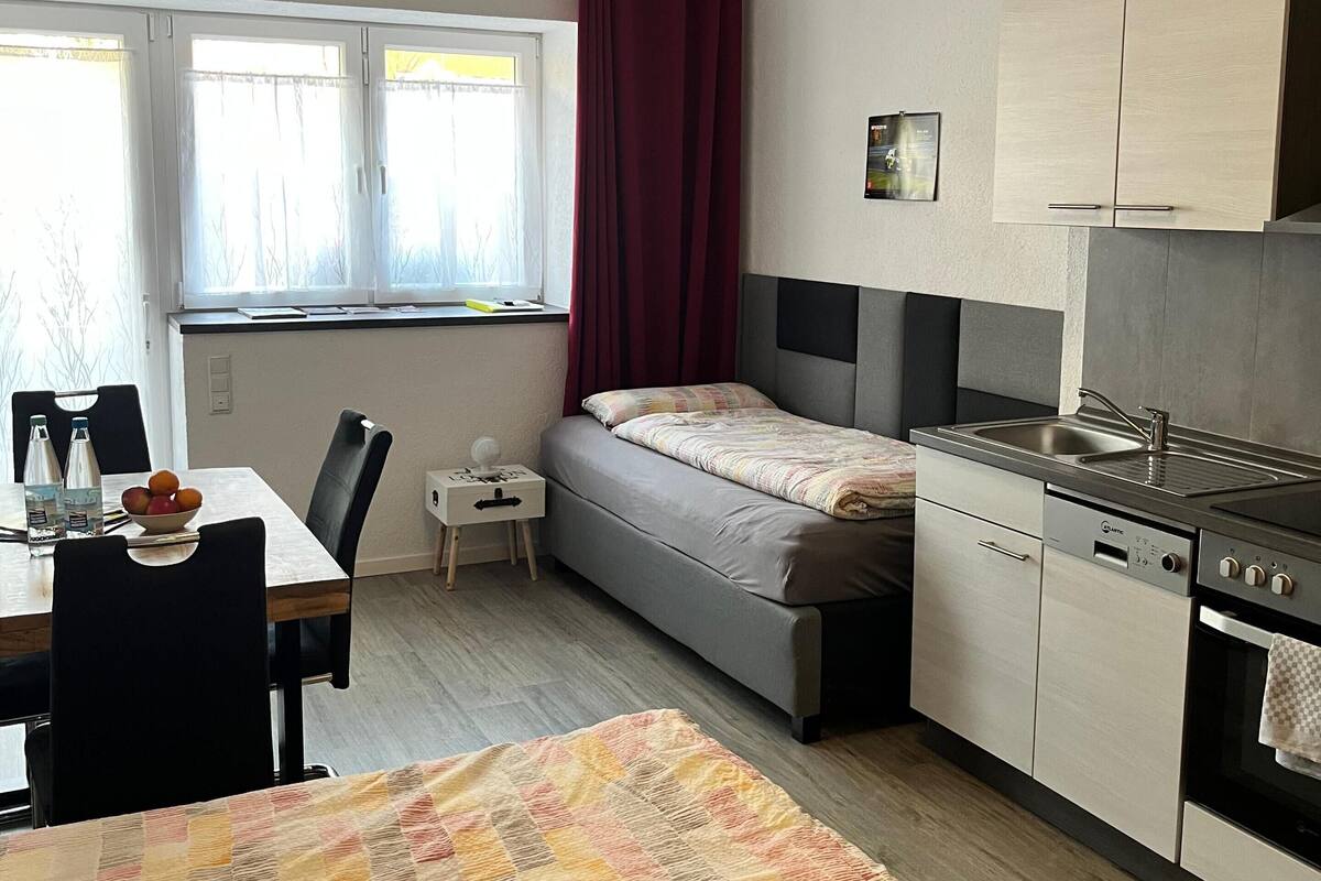 A compact kitchen with a dining area, a bed, and a window with curtains.