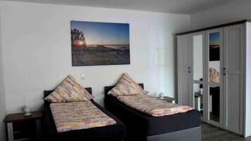A room with two single beds, a wall-mounted picture, a door leading to a closet, and a bedside table with a lamp.