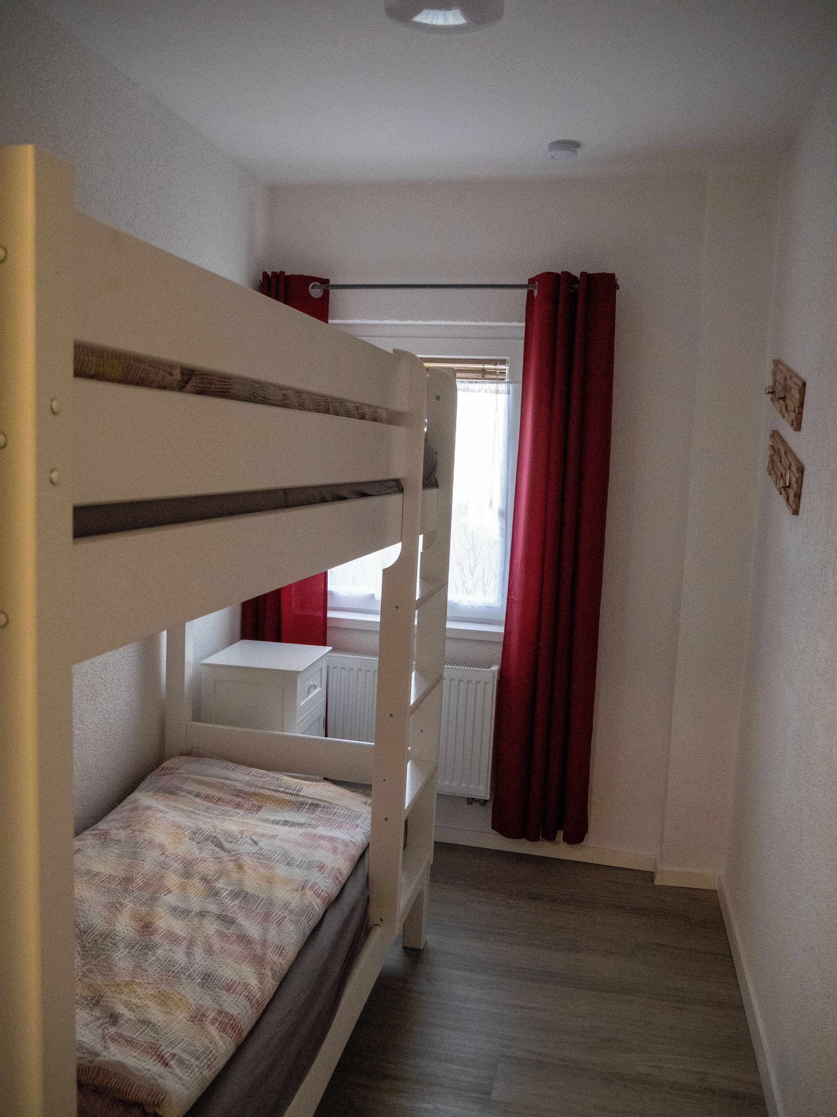 A bunk bed room with a window, red curtains, and a radiator.