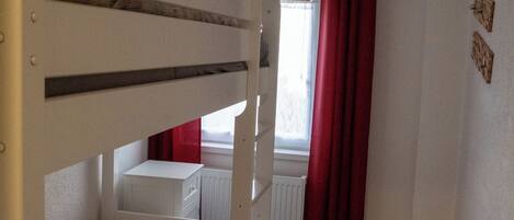 A bunk bed room with a window, red curtains, and a radiator.