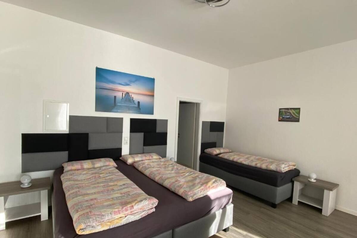 A hotel room with two beds, a nightstand, a desk, a chair, a painting, and a door.