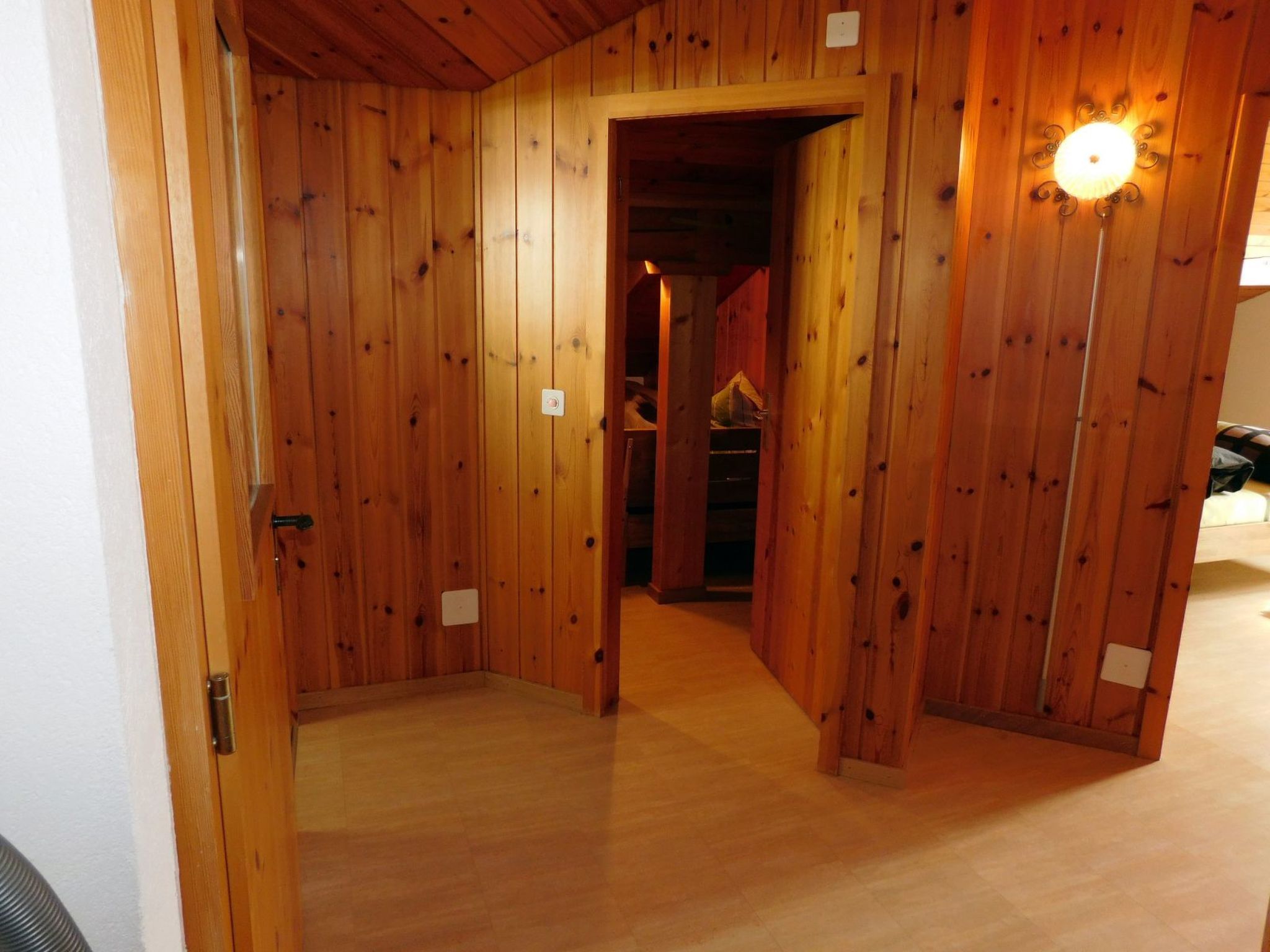 A wooden interior hallway with a door leading to another room.