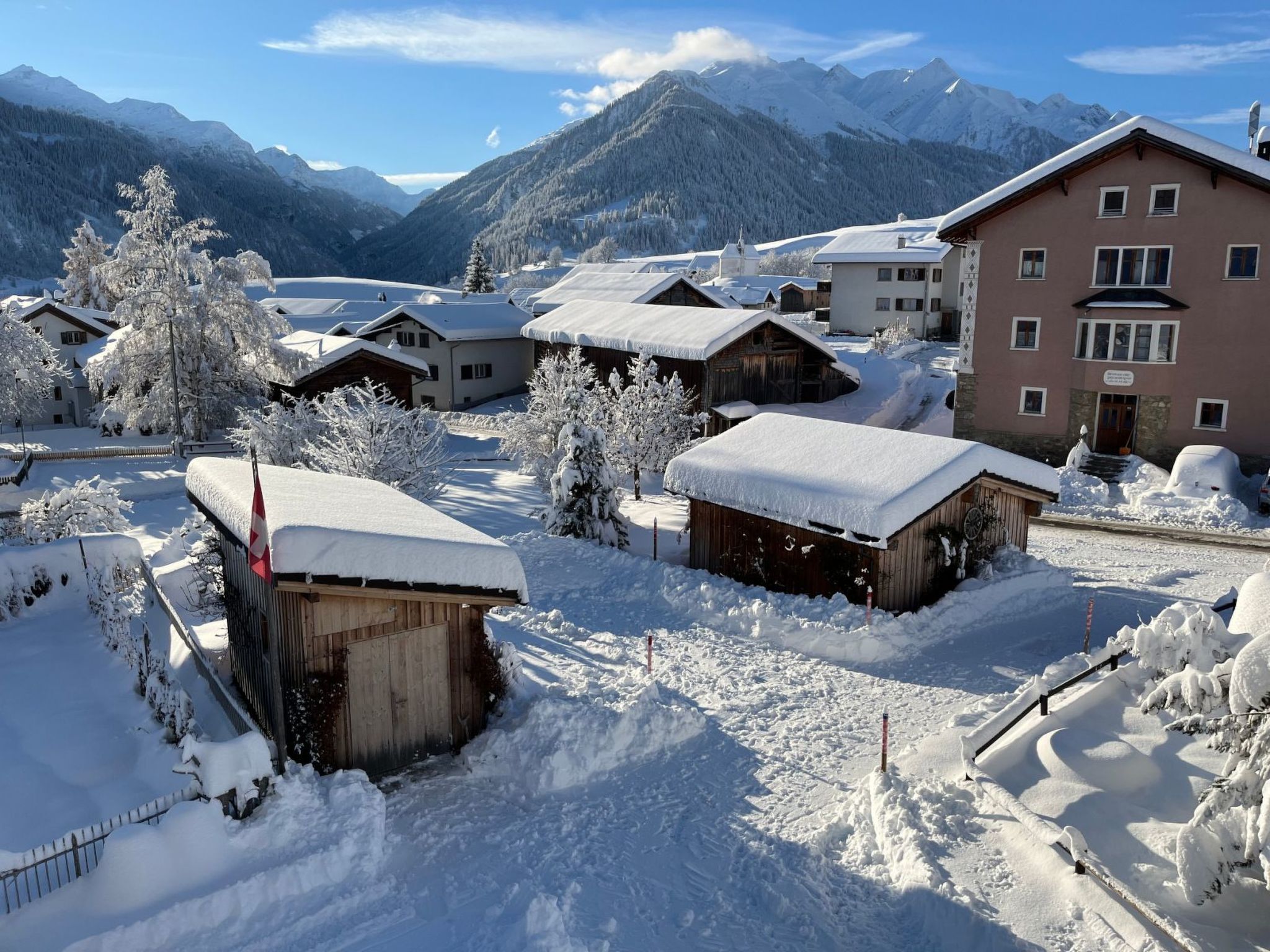 Ein schneebedecktes Dorf mit traditionellen Holzhäusern, einer Seilbahn und Bergen im Hintergrund.