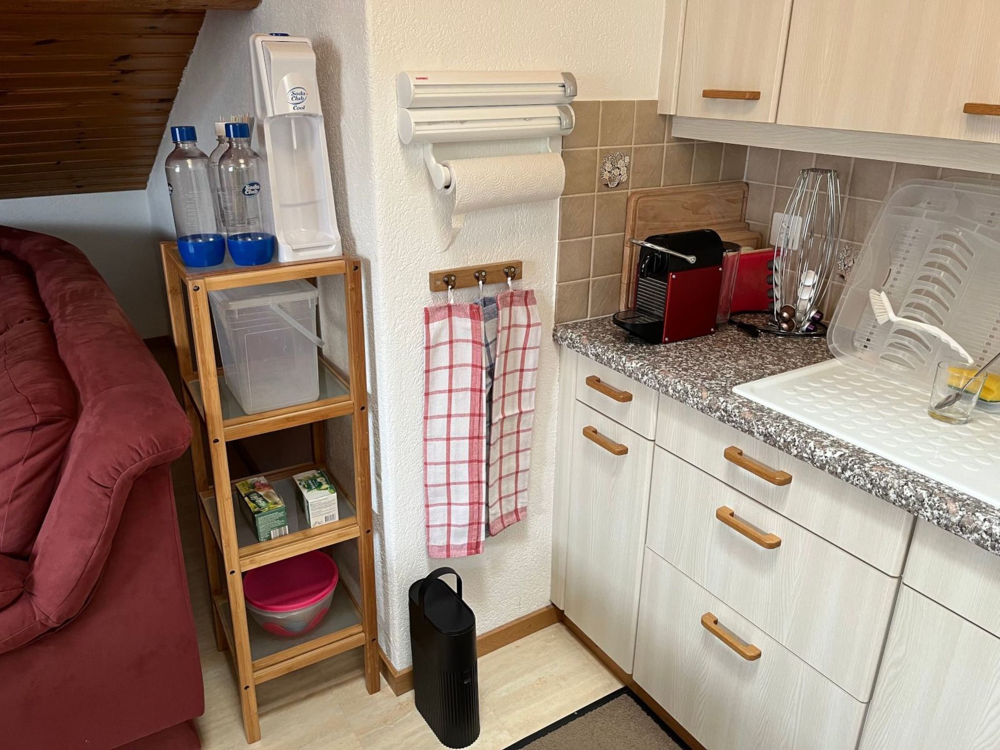 Una cocina compacta con un estante de madera, una silla roja y una encimera con una cafetera.