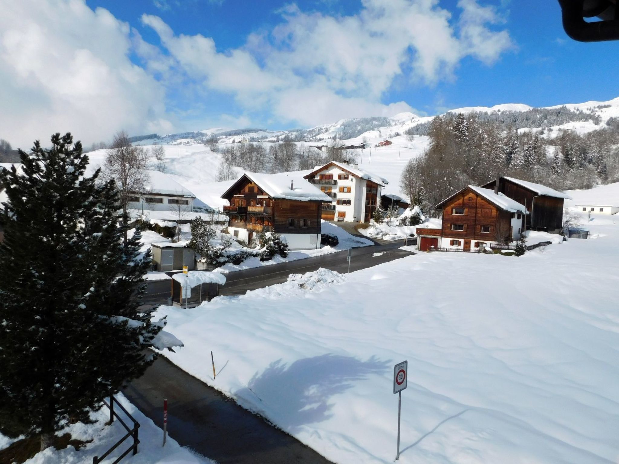 Ein verschneites Dorf mit Holzhäusern, einem klaren Himmel und einem Berg im Hintergrund.