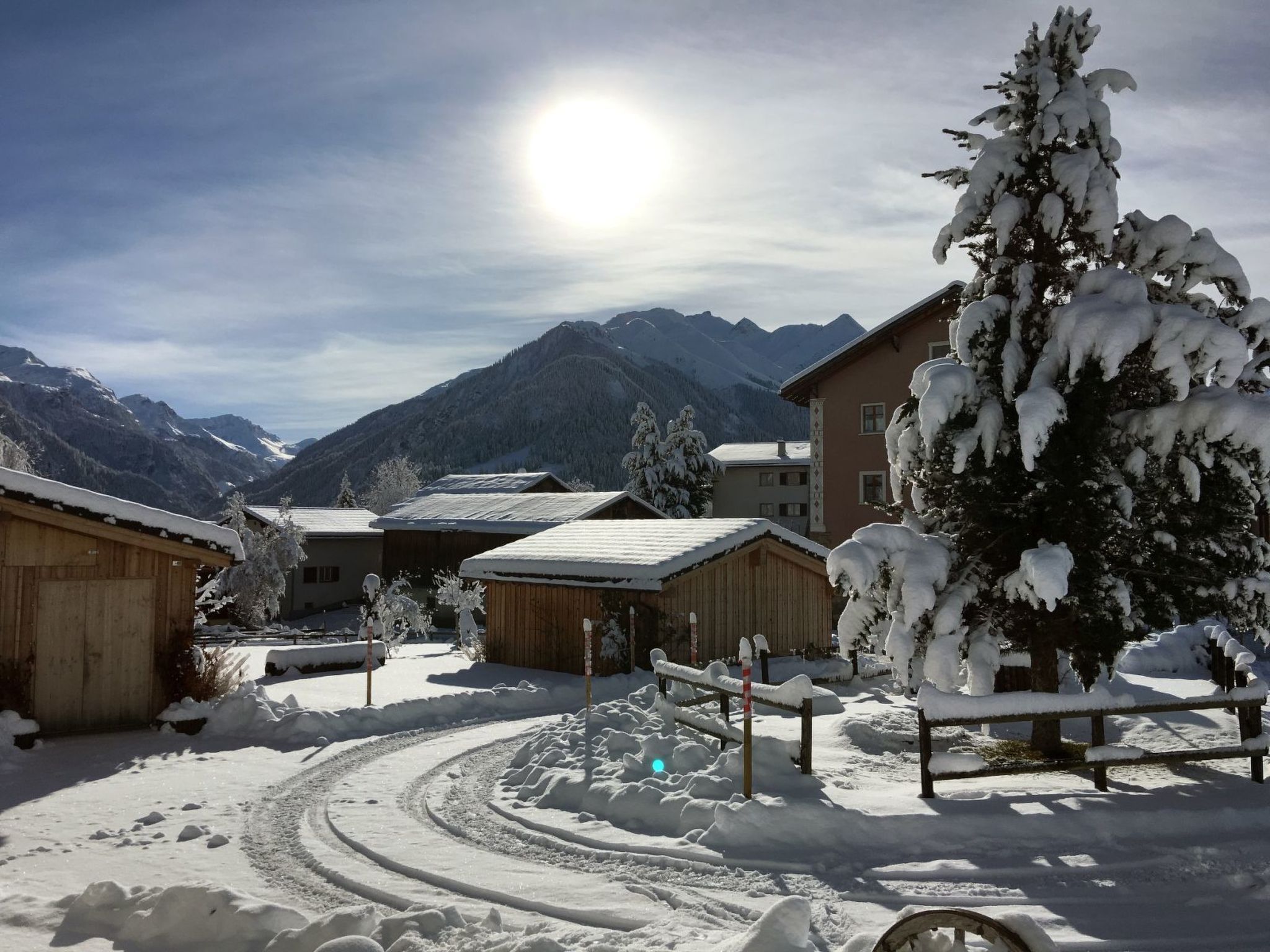 A snow-covered village with wooden buildings, a clear sky, and mountains in the background.