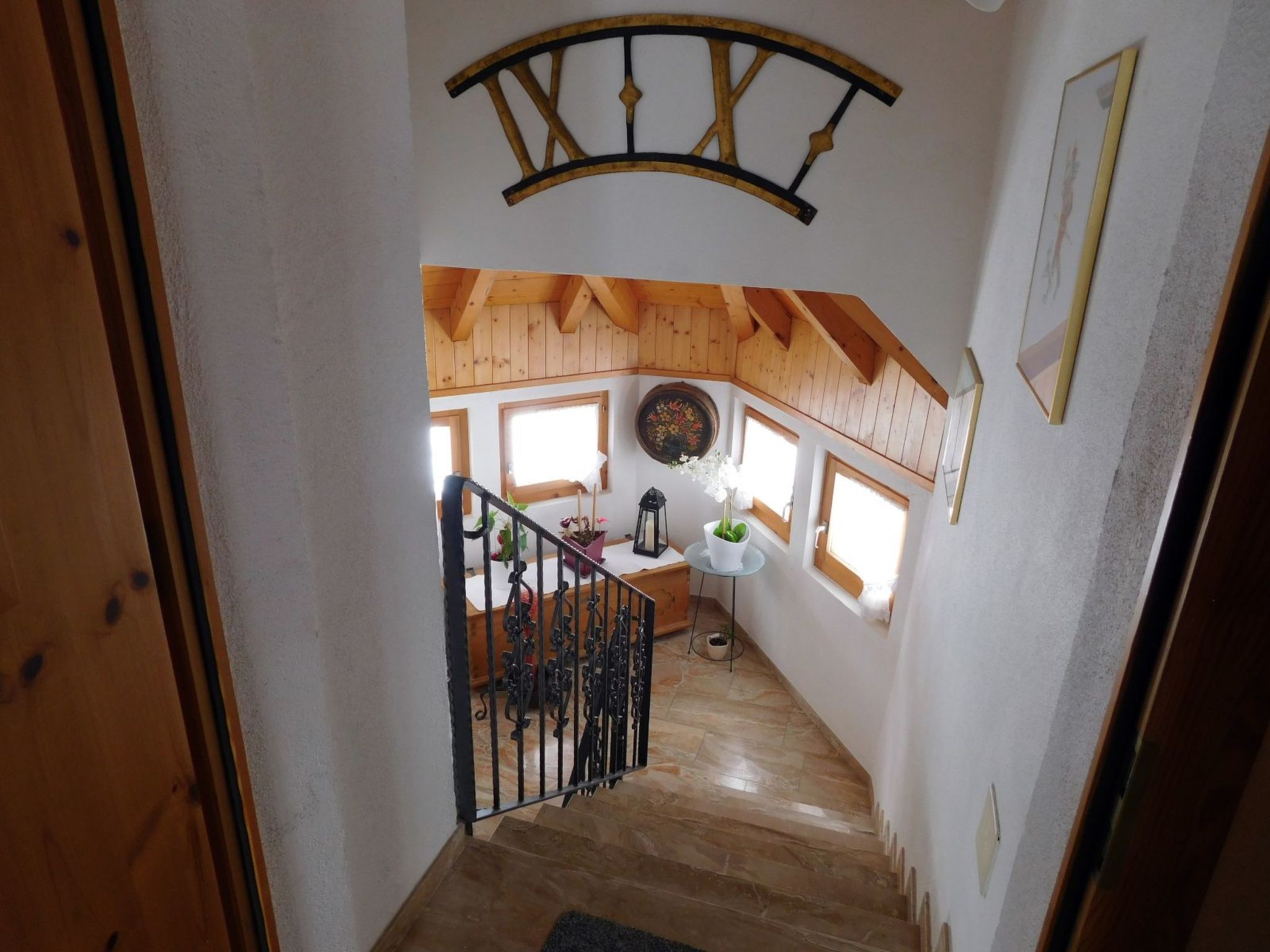 Una scala in legno conduce a una stanza con soffitto in legno, una finestra vista e un orologio appeso al muro.