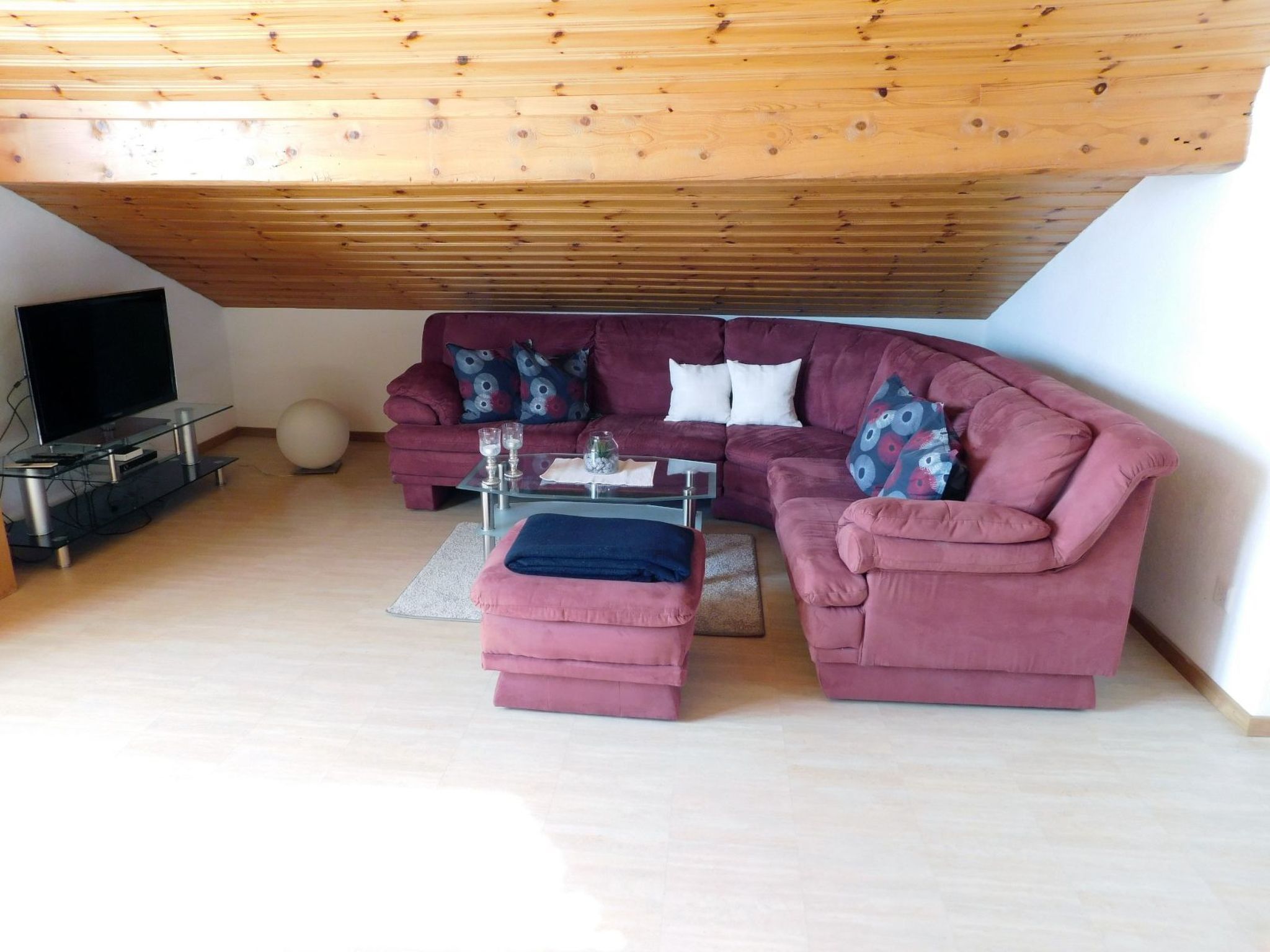 Una sala de estar con un sofá curvo, una mesa de centro de vidrio y un televisor sobre un mueble.