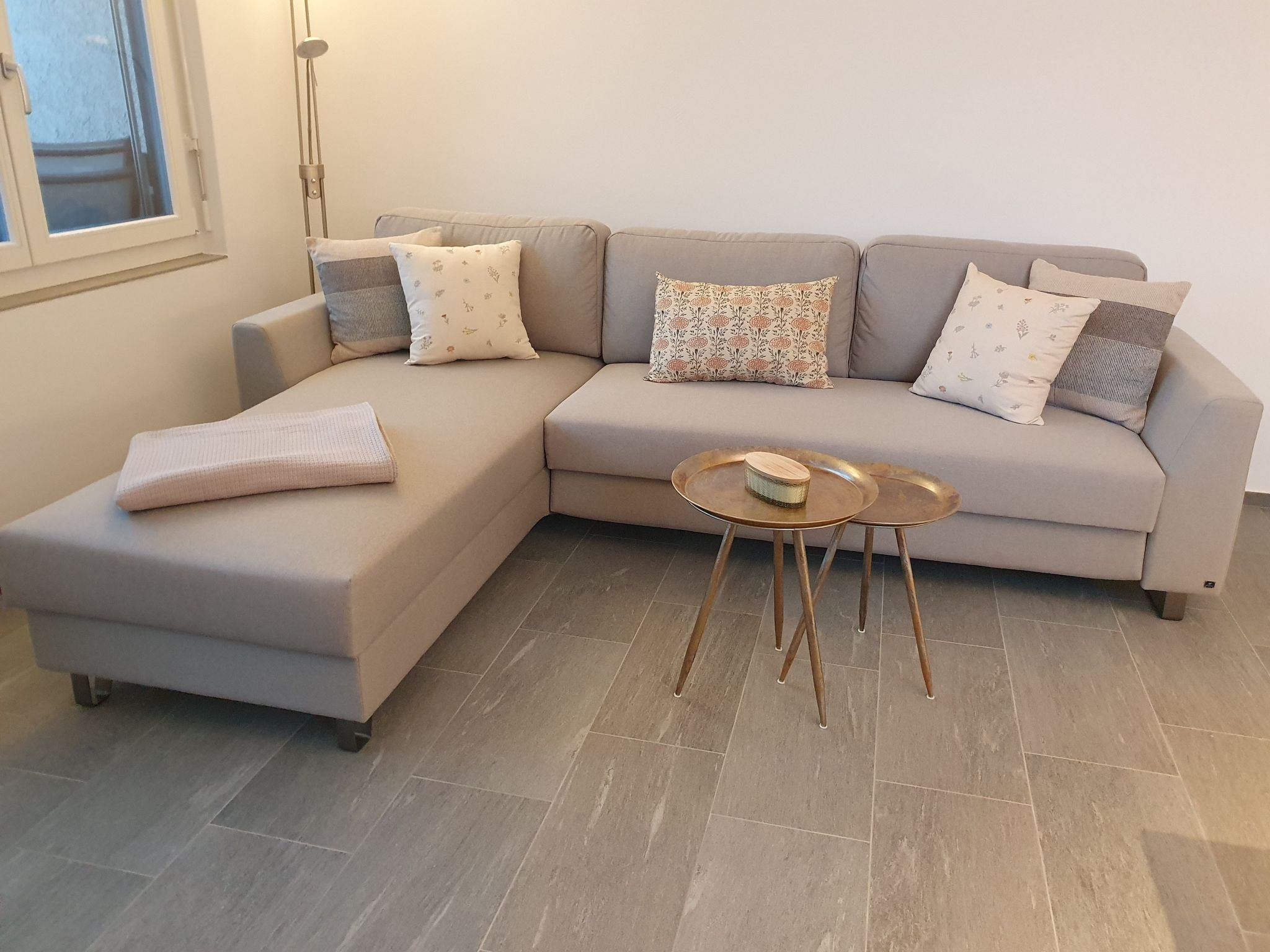 Ein modernes Wohnzimmer mit einer Eckcouch, einem kleinen runden Couchtisch und einer Stehlampe.