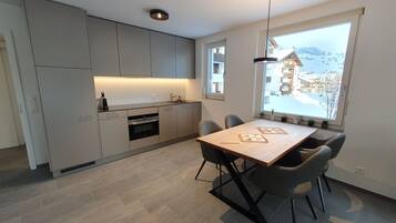 Eine moderne Küche mit grauen Schränken, einem eingebauten Ofen und einer Essecke mit Holztisch und grauen Stühlen.