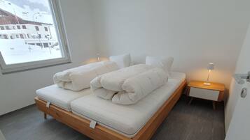 Ein modernes Schlafzimmer mit einem Bett, Nachttischen und Blick auf eine verschneite Landschaft.