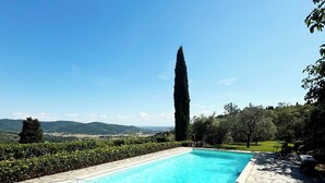 Una piscina con bordo in pietra, immersa nel verde e con vista su colline lontane.