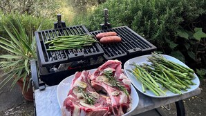 Una griglia con asparagi e salsicce, un piatto con carne cruda, e un lampione in un contesto naturale suggestivo.