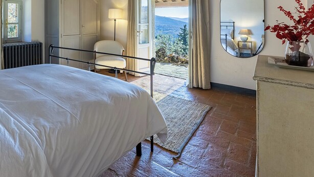 Una camera da letto con un letto, una sedia, una cassettiera, uno specchio e vista sull'esterno.
