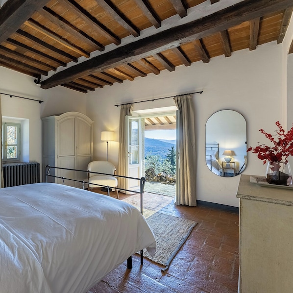 Ein Schlafzimmer mit Bett, Sessel, Kommode, Spiegel und Blick ins Freie.