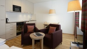 Un espacio habitable compacto con kitchenette, dos sillones, una mesita redonda y comedor.