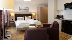 Una habitación de hotel moderna con cama, mesitas de noche, lámpara, silla, una pequeña mesa y una zona de cocina con microondas y un armario.
